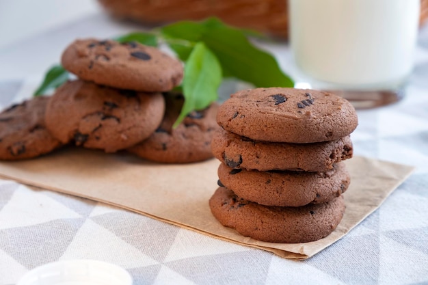 Pila di biscotti con gocce di cioccolato con bicchiere di biscotti al latte e cesto di vimini sullo sfondo Ricetta di delizioso dessert per il tè biscotti appena sfornati con briciole di cioccolato