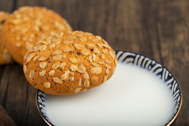 Pila di biscotti di farina d'avena con cereali e semi e ciotola di latte.