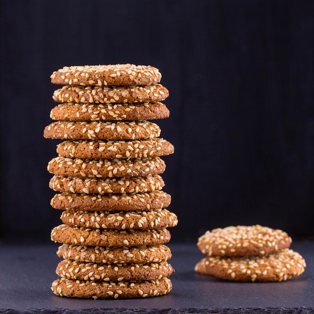 Pila di biscotti fatti in casa biscotti d'avena con semi di sesamo sullo sfondo di ardesia nera da vicino