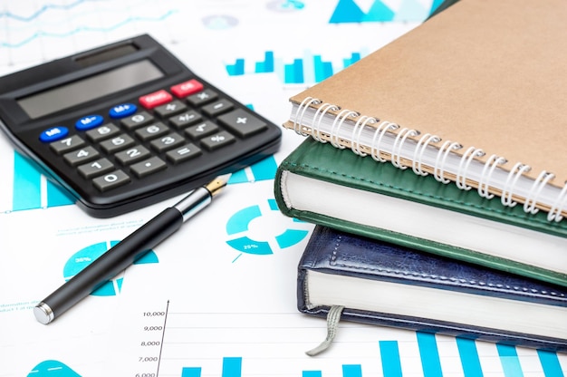 Pila di blocchi note con calcolatrice e penna sui grafici finanziari Concetto di business