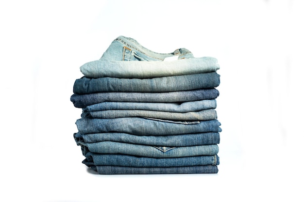 Pila di blue jeans di varie tonalità. Jeans impilati isolati su sfondo bianco. Insegna di struttura dei jeans blu del denim con lo spazio della copia per il fondo di progettazione del testo. Tela denim moda texture