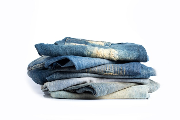 Pila di blue jeans di varie tonalità. Jeans impilati isolati su sfondo bianco. Insegna di struttura dei jeans blu del denim con lo spazio della copia per il fondo di progettazione del testo. Tela denim moda texture