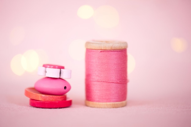 Pila di bottoni colorati con filo di cotone rosa su luci sullo sfondo. Messa a fuoco selettiva.