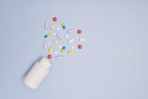 Pila di capsule mediche pillole in colore rosso e bianco su sfondo blu, vista dall'alto per lo spazio della copia. Pillole e compresse mediche bianche che si rovesciano da una bottiglia della droga. Vista dall'alto verso il basso macro con lo spazio della copia.