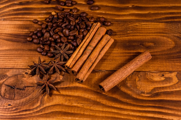 Pila di chicchi di caffè, anice stellato e bastoncini di cannella su tavola in legno rustico