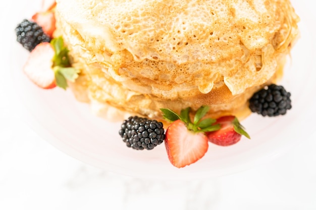 Pila di crepes appena sfornate con frutti di bosco su un supporto per torta.