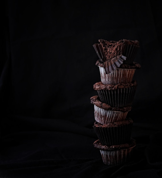 pila di cupcakes al cioccolato in involucri di carta su sfondo nero