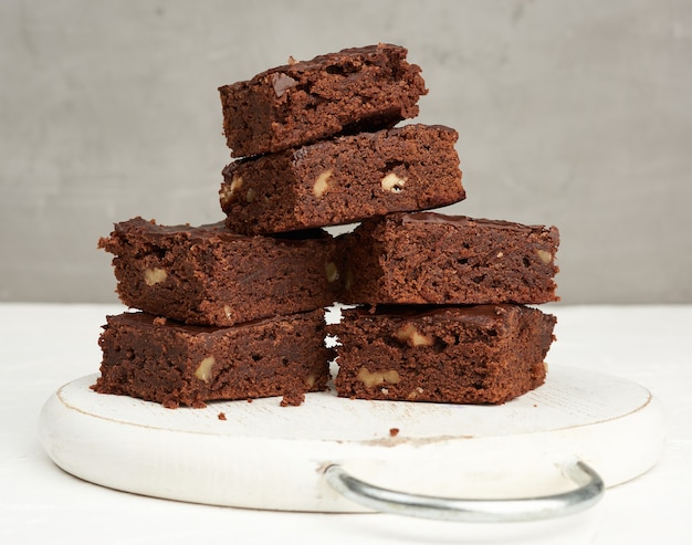 Pila di fette al forno quadrate di torta al cioccolato brownie con noci