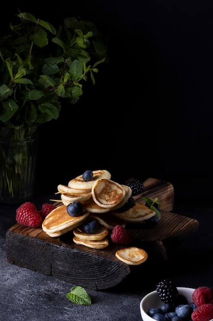 Pila di frittelle con frutti di bosco su tavola di legno. Fondo in legno scuro.