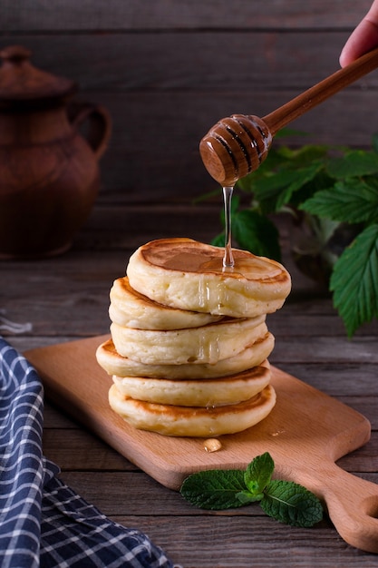 Pila di frittelle con sciroppo di miele su sfondo scuro in legno. Colazione salutare