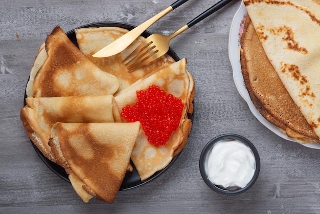 Pila di frittelle russe sottili blini con caviale rosso e panna acida fresca