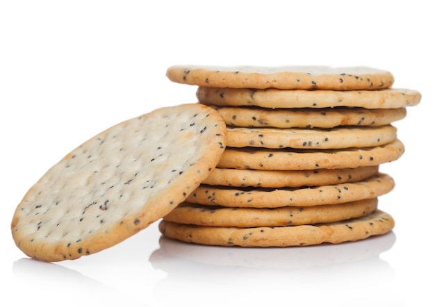 Pila di grano croccante organico rotondo e cracker salati di cinque grani con i semi su fondo bianco.