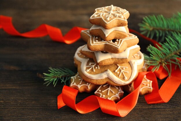 Pila di gustosi biscotti di panpepato, nastro e ramo di albero di Natale su sfondo di legno, vista ravvicinata