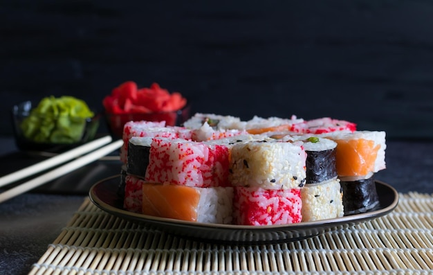 Pila di involtini di sushi con wasabi e zenzero su piatto nero e sfondo scuro