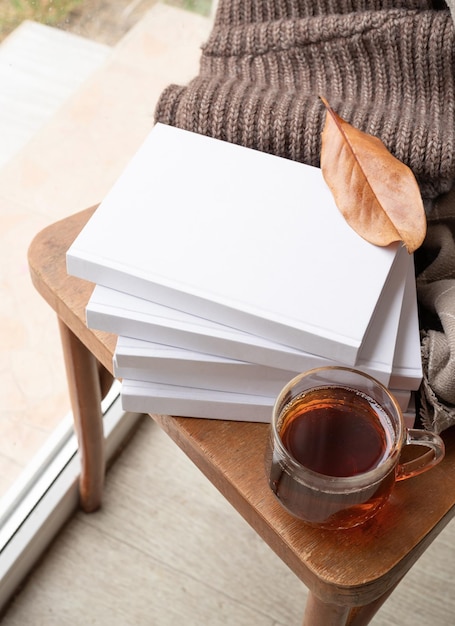Pila di libri in bianco bianchi con foglie autunnali e tazza di tè caldo sul vecchio design del modello di sedia in legno