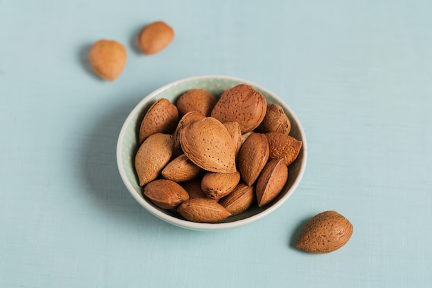 Pila di mandorle noci in una ciotola su uno sfondo azzurro. Noci fresche nel loro guscio.