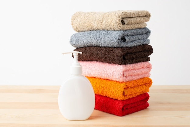 Pila di nuovi asciugamani colorati con bottiglia di sapone sul tavolo di legno