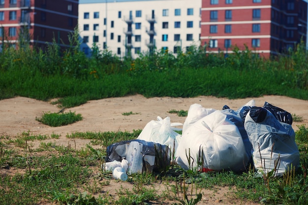 Pila di pacchetti di immondizia su un terreno contro il multi condominio sfocato. Rifiuti di plastica. Concetto di problema di riciclaggio dei rifiuti e smaltimento dei rifiuti.