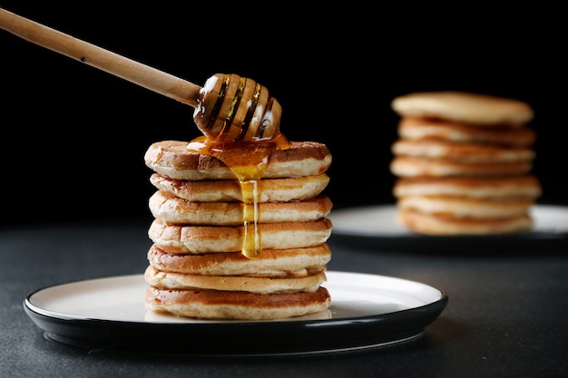 Pila di pancake con miele di versamento su fondo scuro. decorazione e colazione