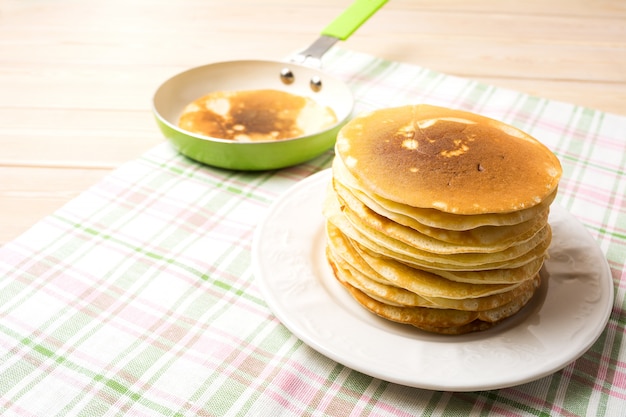 Pila di pancake della prima colazione sul piatto bianco e sulla pentola verde