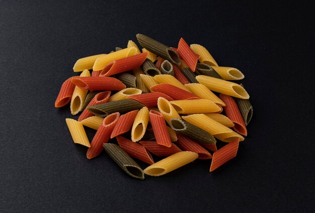 Pila di penne rigate colorate, mix di pasta colorata isolato su sfondo nero