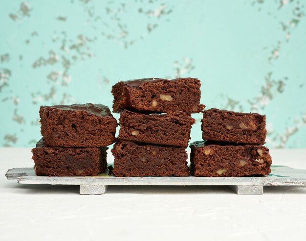 Pila di pezzi al forno quadrati di dolce al cioccolato del brownie con le noci su un bordo di legno