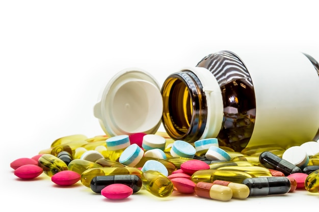 Pila di pillole di medicina e capsule di farmaci con bottiglie di pillola su sfondo bianco.
