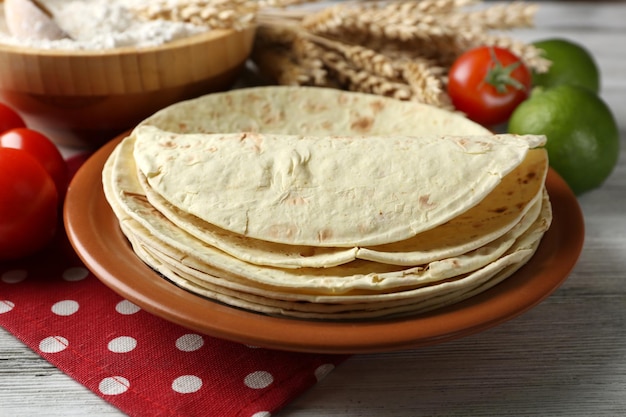 Pila di tortilla di farina di grano intero fatta in casa e verdure sul piatto sul fondo della tavola in legno