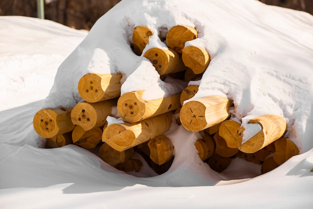 Pila di tronchi di legno giacciono a terra sotto la neve durante la raccolta invernale per una casa ecologica