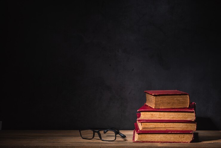 Pila di vecchi libri e vetri sulla tavola di legno sulla parete nera del cemento