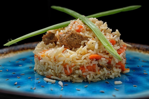 Pilaf uzbeko con carne su un piatto blu, su uno sfondo scuro