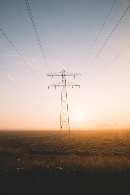 Pilastro elettrico sul campo contro il cielo durante il tramonto