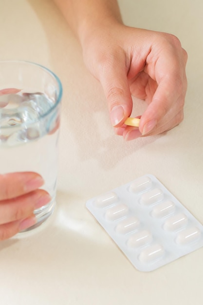 Pillola gialla e un bicchiere d'acqua nelle mani femminili sul concetto di salute della scrivania