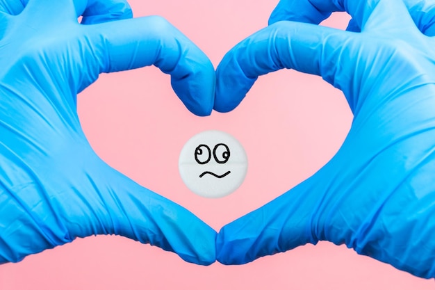 Pillola medica con un'emoticon pazza nel cuore dalle mani su sfondo blu Concetto di droga