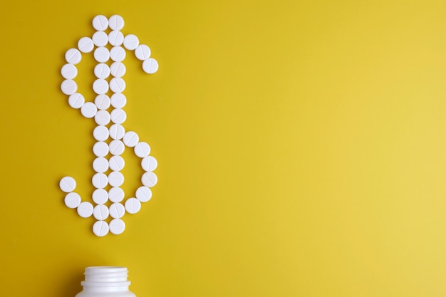 Pillola. Pillole bianche su uno sfondo giallo sotto forma di un segno di dollaro da un vaso bianco