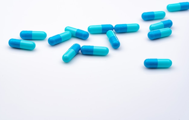 Pillole capsule blu sparse su sfondo bianco. Industria farmaceutica.