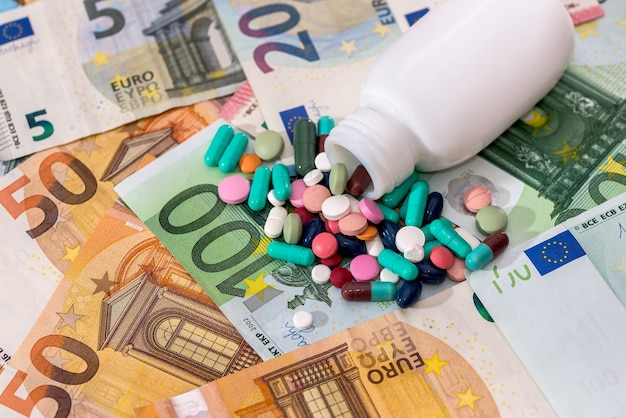 Pillole colorate con contenitore su banconote in euro closeup