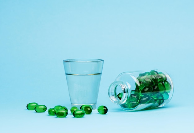 Pillole di capsule mediche e acqua di vetro su sfondo blu