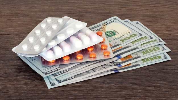 Pillole e dollari su uno sfondo di legno. Pagamento per medicinali