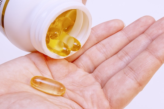 Pillole gialle dell'olio di pesce Omega 3 in una mano. Concetto di vitamine sport sano.