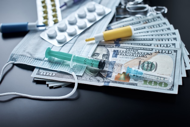 Pillole, maschera protettiva, oggetti medici e banconote da un dollaro su sfondo scuro. Concetto di medicina costoso. Industria farmaceutica e assicurazione medica