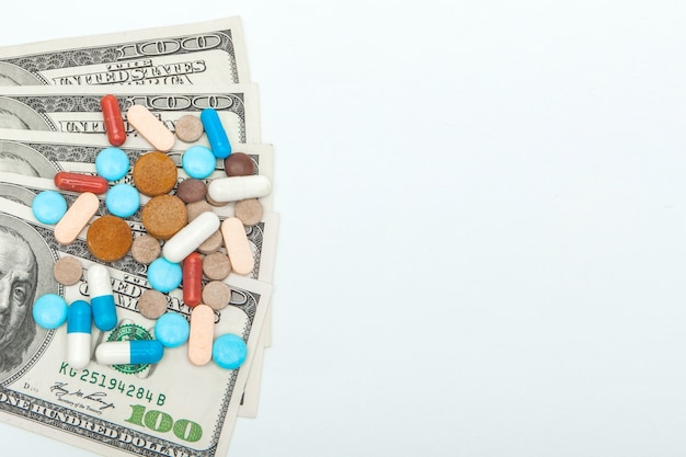 Pillole medicinali colorate e dollari americani su uno sfondo bianco.