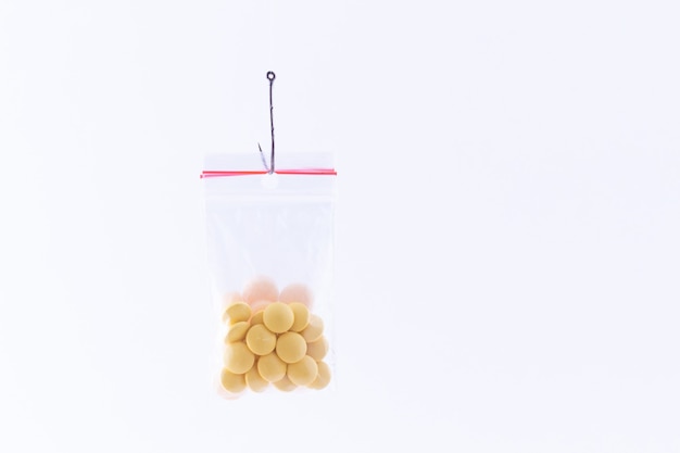 Pillole o compresse colorate appese in una piccola borsa a chiusura lampo su un amo da pesca