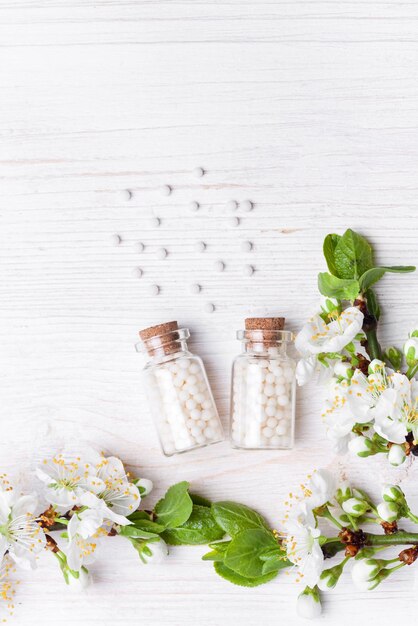 Pillole omeopatiche con fiori di primavera su legno bianco backgroundxAxA