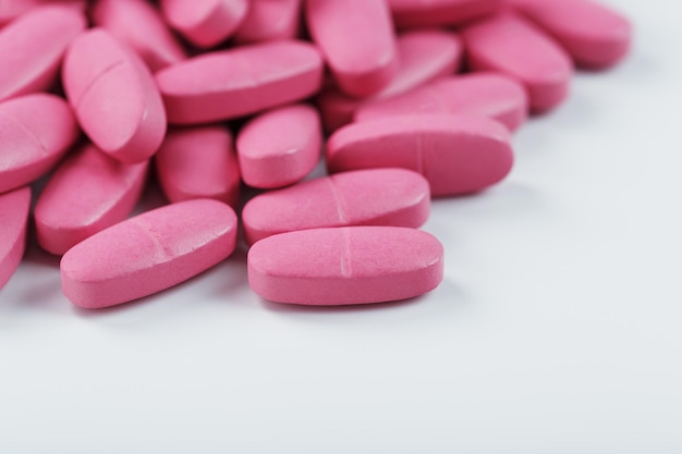 Pillole rosa con multivitaminici su sfondo bianco. Spazio libero