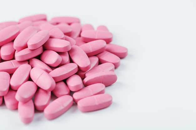 Pillole rosa con multivitaminici su sfondo bianco.