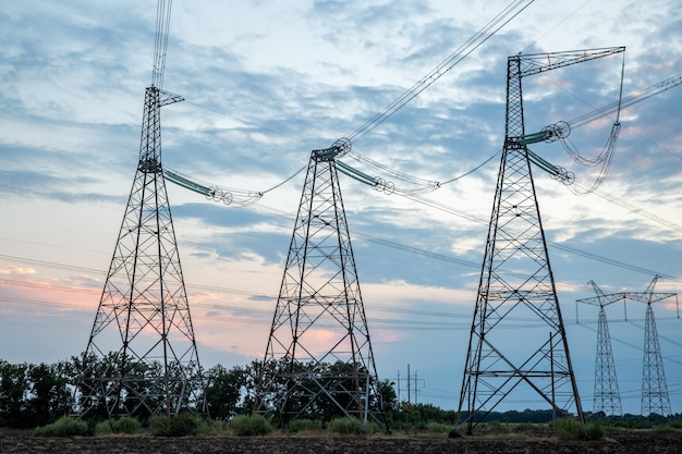 Piloni elettrici e linee elettriche ad alta tensione al tramonto sfondo gruppo silhouette di trasmissione