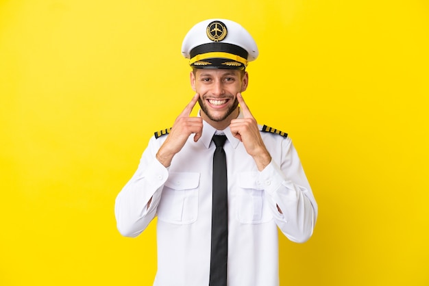 Pilota caucasico dell'aeroplano isolato su sfondo giallo sorridente con un'espressione felice e piacevole