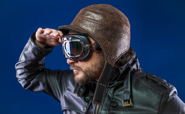 pilota degli anni '20 con occhiali da sole e casco da aviatore vintage. Indossa giacca di pelle, barba e volti espressivi