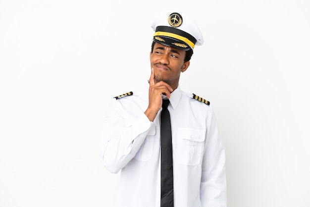 Pilota di aeroplano afroamericano su sfondo bianco isolato pensando a un'idea mentre guarda in alto